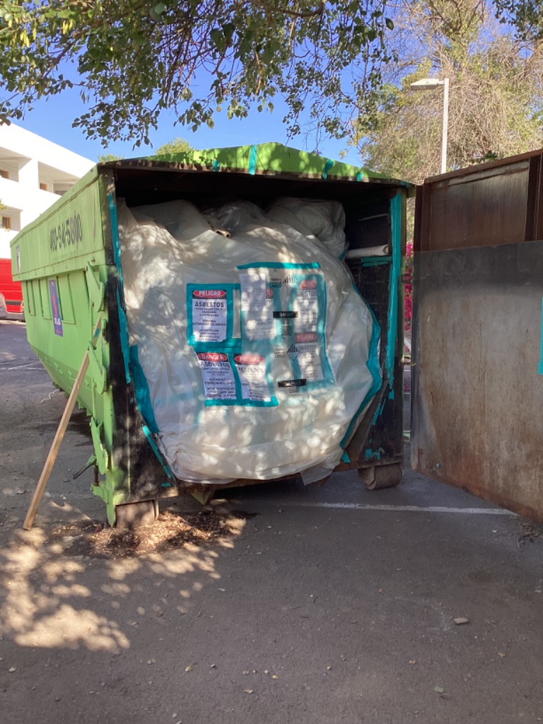 Bagged asbestos-containing waste staged in a labeled dumpster